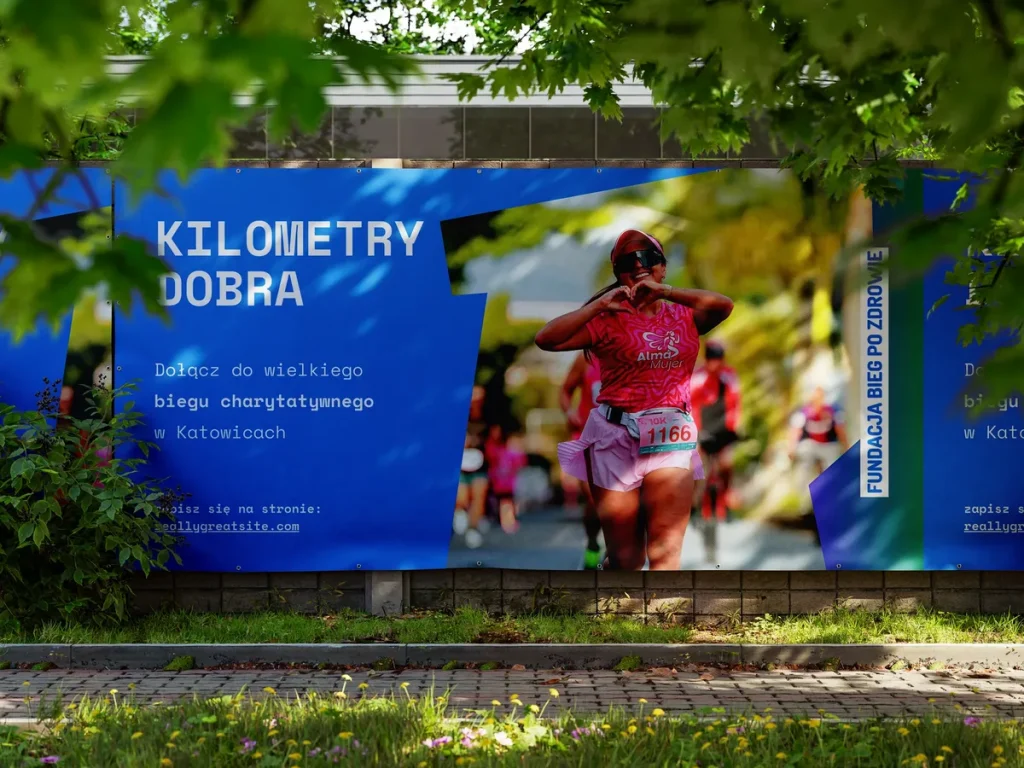 Baner biegu charytatywnego Kilometry dobra rozpięty na ogrodzeniu w parku
