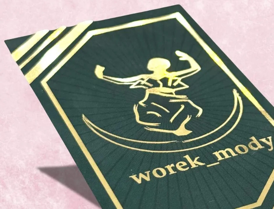 Zielona wizytówka ze złotym logo i napisem wykonanym złoceniem, na różowym tle