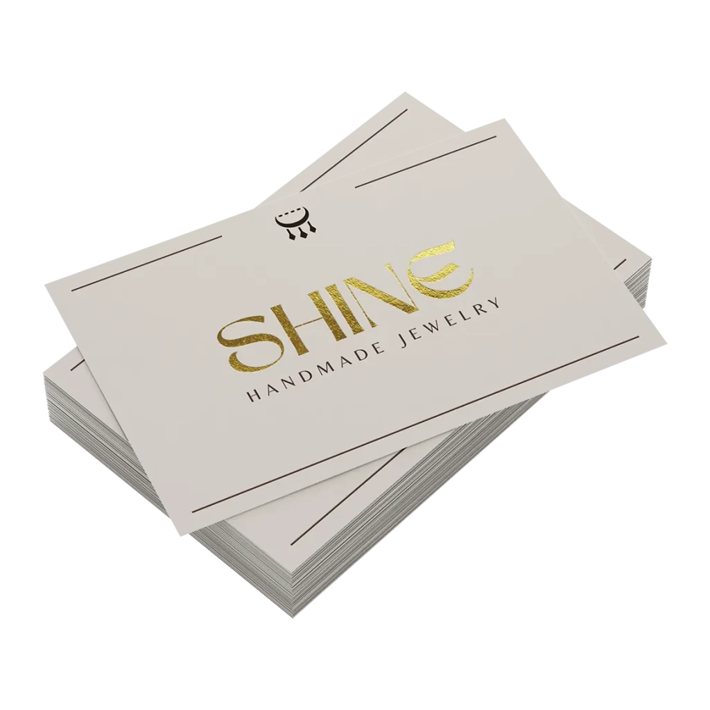 Wizytówki ze złoceniem, złoty napis Shine na kremowym papierze, stos wizytówek